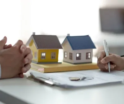 A small model house on a desk beside a signed contract and keys