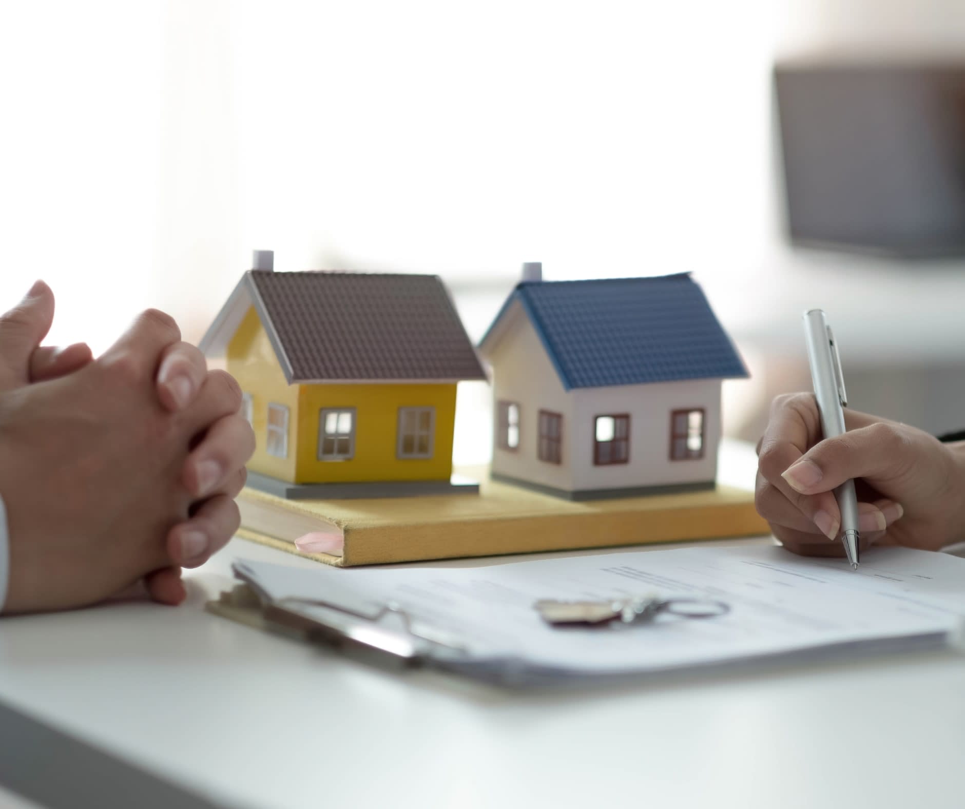 A small model house on a desk beside a signed contract and keys